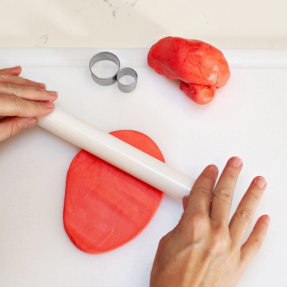 person rolling out a ball of red fondant